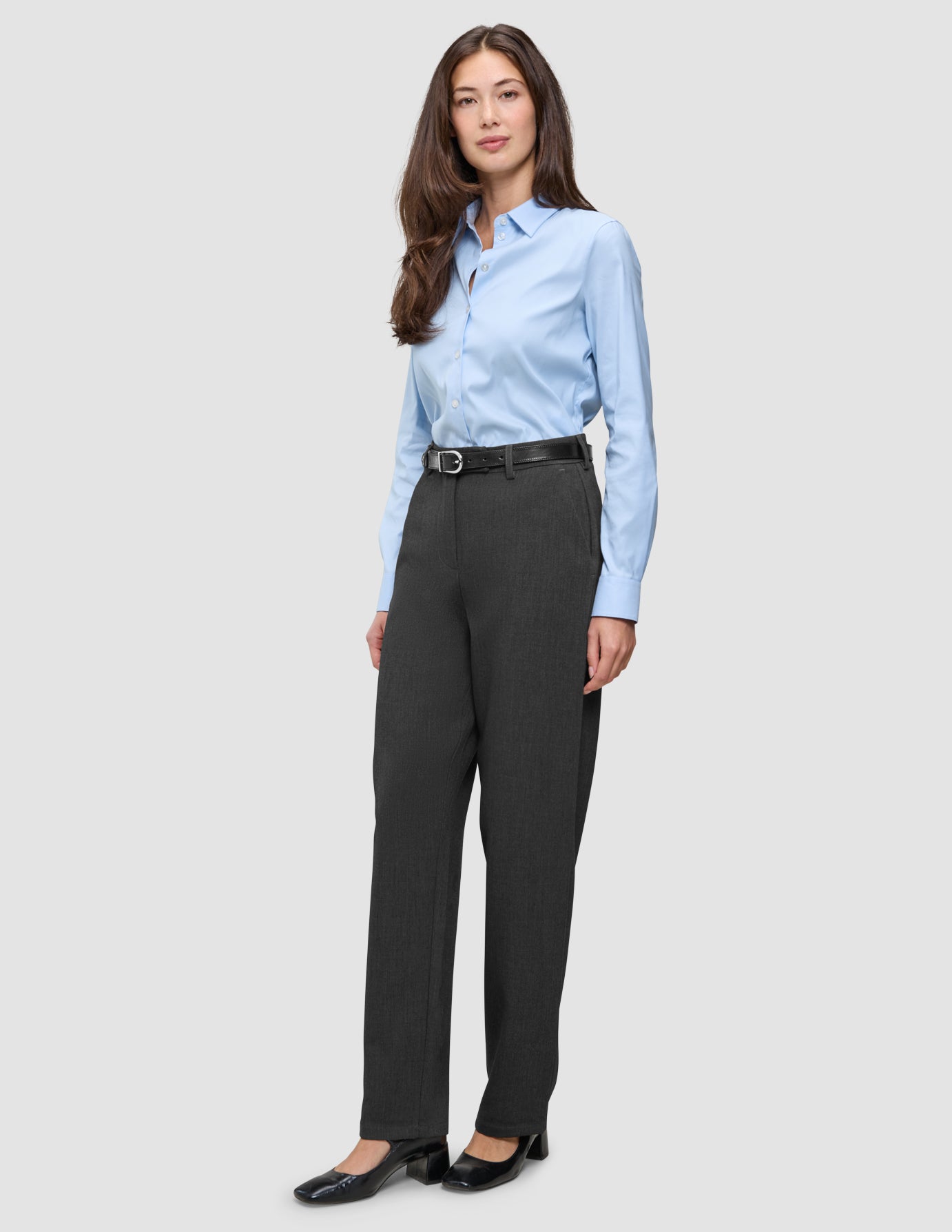 Eine Frau, die ein hellblaues Hemd trägt, das in eine Women GO2 Pants Straight Dark Grey Melange gesteckt ist, dazu einen schwarzen Gürtel und schwarze Pumps – ein klares, skandinavisches Design.